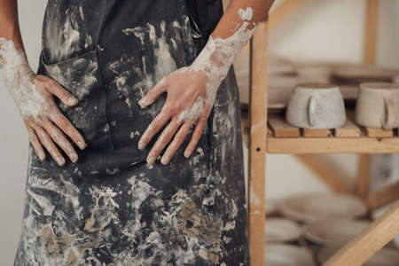 Unrecognisable Female Potter Dressed in Apron that Greased in Clay Standing Near Her Works in Pottery Studioの写真素材