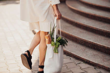 Back View of Unrecognisable Stylish Woman Holding Shopping Eco Bag with Groceries Outdoors While Walking on the Streetの写真素材