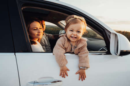 little Girl Looking Out of Car Window, Young Family with Baby Daughter on a Road Trip at Sunsetの写真素材