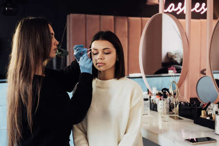 Female Master Combs the Eyebrow to Young Woman, Process of Cleaning Procedure at Beauty Salonの写真素材