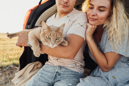 Young Woman and Man Sitting in Trunk of the Car with Pet, Happy Couple with Their Red Cat Enjoying Road Tripの写真素材