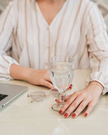 Close Up of Unrecognisable Woman Sitting by a Table with Laptop, Glass of Water and Glassesの写真素材