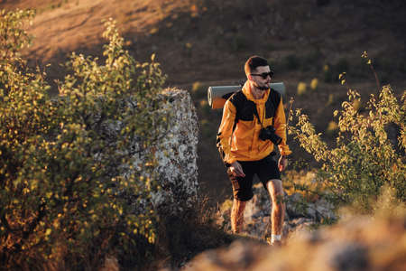 Male Hiker with Backpack and Digital Camera Walking on the Hill During Sunset, Traveler Man in Solo...