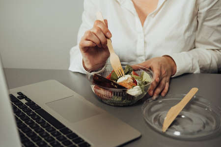 Unrecognisable Female Employee Having Lunch in the Office, Woman Eating Salad at Working Placeの写真素材