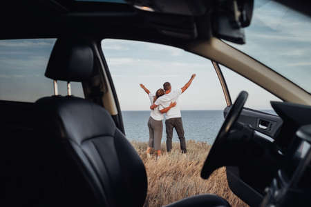 View From Car Interior, Young Couple on a Road Trip, Man and Woman Embracing on Sea Backgroundの写真素材