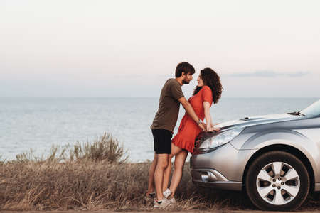 Young Lovers Man and Woman Standing Together Near Their SUV Car on Background of the Sea at Sunsetの写真素材