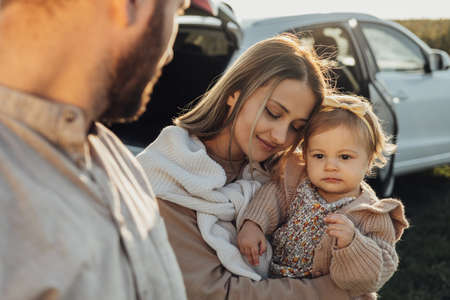 Young Caucasian Family Enjoying Road Trip, Mother and Father with Little Daughter Outdoors with SUV Car on the Backgroundの写真素材
