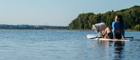 Young Woman Relaxing on the City Lake While Sitting on the Sup Board with Her Dog Japanese Spitzの写真素材