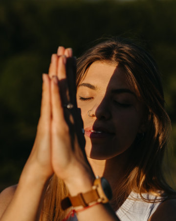Close Up Portrait Young Woman Practicing Yoga and Meditation with Folded Hands Outdoors at Sunsetの写真素材