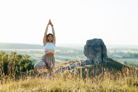 Young Woman Meditating and Practicing Yoga Outdoors at Sunset with Scenic Landscape and Nature Miracle Giant Stone on the Backgroundの写真素材