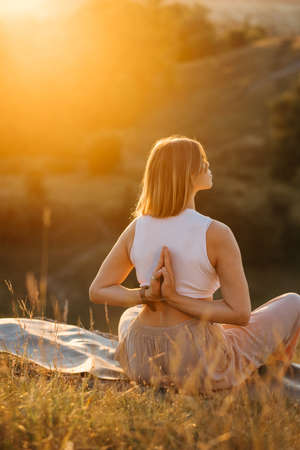 Young Woman with Folded Hands on the Back Meditating and Enjoying Beautiful Sunset Outdoorsの写真素材