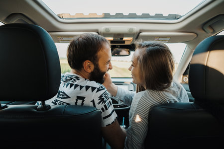 Happy middle-aged couple enjoying road trip together, cheerful caucasian man and woman sitting inside the SUV car while on vacationの写真素材