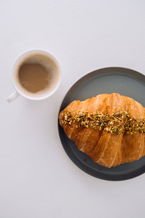 Flat lay of cup of cappuccino with pistachio croissant on the white tableの写真素材