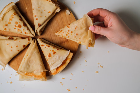Womans hand holding delicious crepe, crepes laid out in triangles in a circle on a wooden board,...