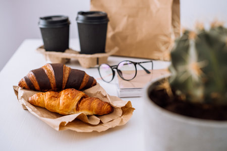 Delicious brown and chocolate croissants with coffee cups, having lunch at workplace, food delivery conceptの写真素材