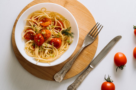 Flat lay portion of spaghetti pasta with cherry tomatoes sprinkled with spices in a plate on a wooden boardの写真素材