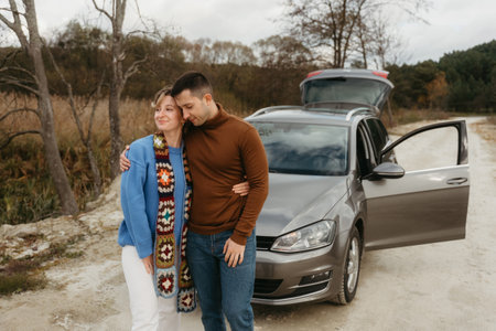A man and woman by a car on a dirt road, adult couple on autumn roadtripの写真素材