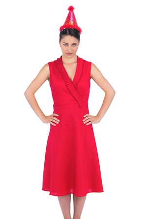 Serious gorgeous brunette in red dress on white background wearing party hatの写真素材