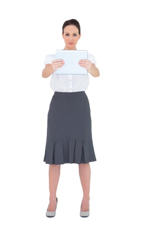 Serious businesswoman holding her tablet pc while posing on white backgroundの写真素材