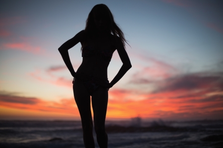 Silhouette of slim woman posing on the beach at duskの写真素材