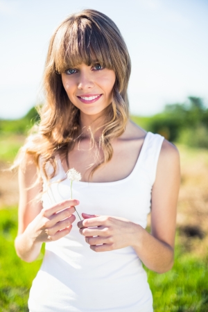Smiling pretty blonde holding dandelion walking on grassland on a summers dayの写真素材