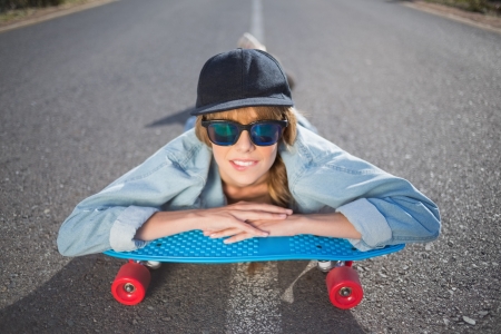 Funky young blonde lying on a deserted road with her skateboardの写真素材