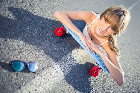 Funky young blonde lying on the road on her skateboard smilingの写真素材