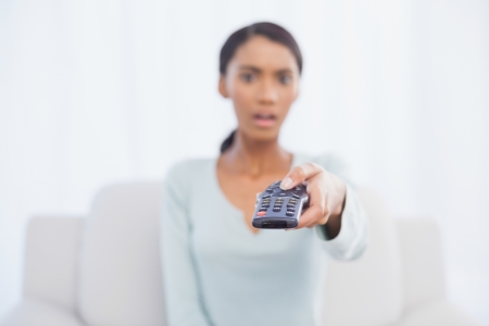 Shocked woman sitting on sofa in bright living room changing tv channelの写真素材