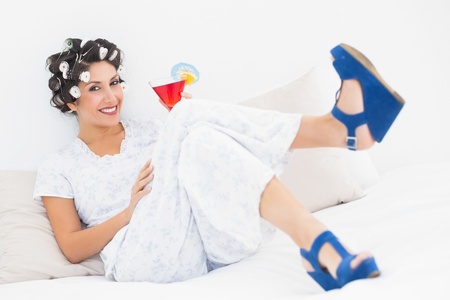Brunette in hair curlers and wedge shoes holding a cocktail in bedroom at homeの写真素材
