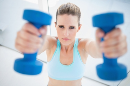 Serious woman exercising with dumbbells looking at cameraの写真素材