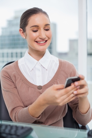 Smiling beautiful businesswoman in bright office text messagingの写真素材