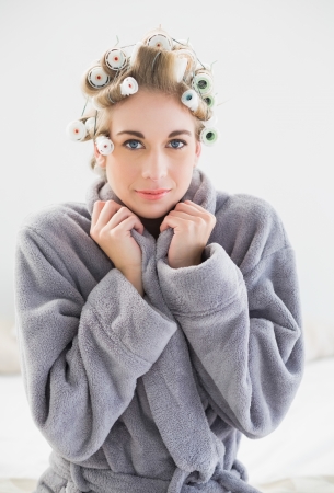 Lovely relaxed blonde woman in hair curlers looking at camera in a bedroomの写真素材