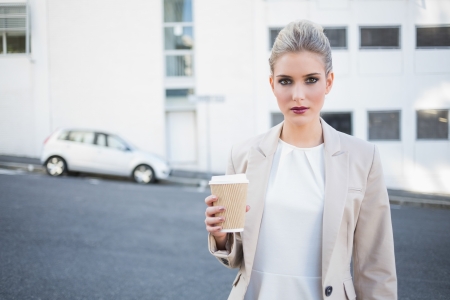 Serious stylish businesswoman holding coffee outside on urban backgroundの写真素材