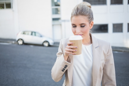 Peaceful stylish businesswoman smelling coffee outside on urban backgroundの写真素材
