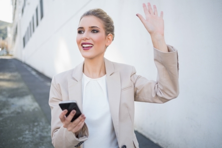 Cheerful attractive businesswoman waving outdoors on urban backgroundの写真素材