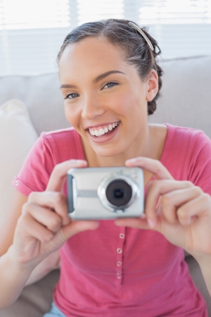 Cheerful woman in living room taking pictures while looking at cameraの写真素材
