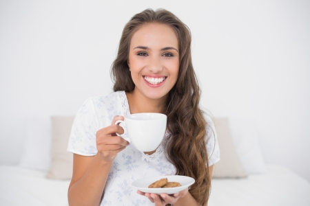 Cheerful attractive brunette holding a cup in bright bedroomの写真素材