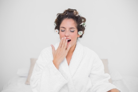 Yawning natural brunette closing her eyes and sitting on bedの写真素材