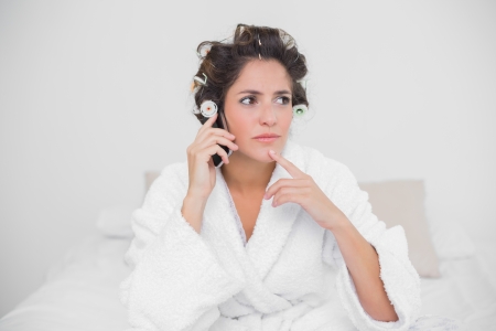 Pensive natural brunette phoning and sitting on bedの写真素材
