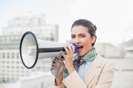 Irritated smart brown haired businesswoman using a megaphone outdoorsの写真素材