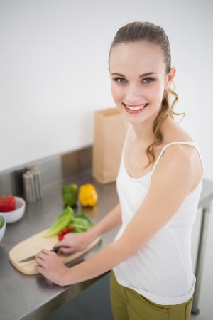 Happy young woman preparing vegetables smiling at camera in the kitchen at homeの写真素材
