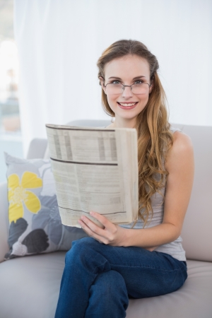 Cheerful young woman sitting on sofa holding newspaper at home in the sitting roomの写真素材