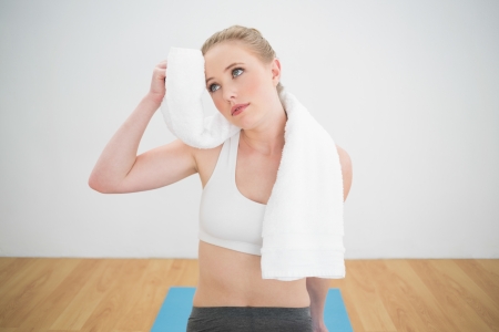 Thoughtful sporty blonde touching forehead with towel in bright roomの写真素材