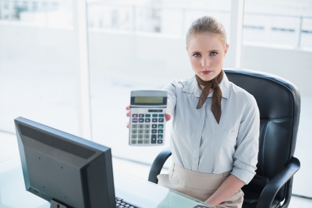 Blonde serious businesswoman showing calculator in bright officeの写真素材
