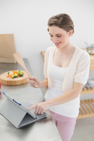 Smiling brunette woman using her tablet while standing in her kitchen at homeの写真素材