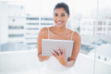 Cheerful toned brunette holding tablet in bright roomの写真素材