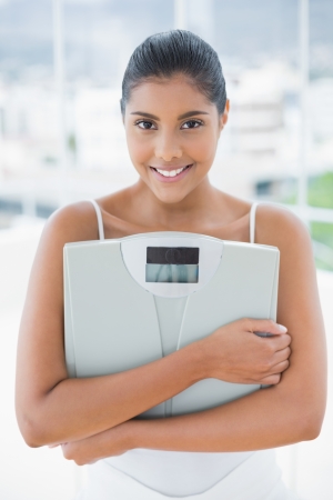 Smiling toned brunette holding scales in bright roomの写真素材
