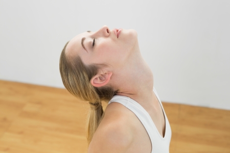 Young toned woman kneeling on floor in sports hall stretching with eyes closedの写真素材