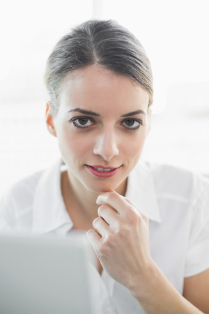 Content thinking businesswoman smiling softly at camera sitting at her deskの写真素材