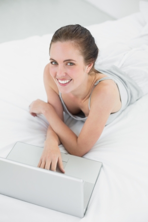 Portrait of a smiling casual young woman using laptop in bed at homeの写真素材